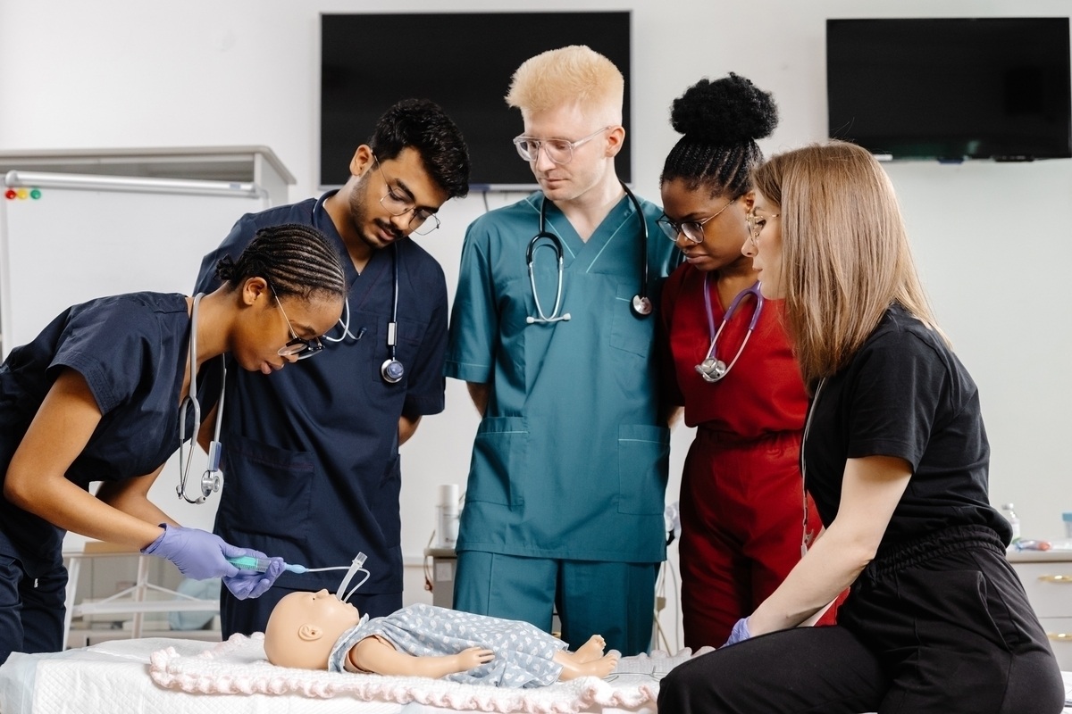 Healthcare students in scrubs practicing clinical skills on a mannequin during CNA training in New York