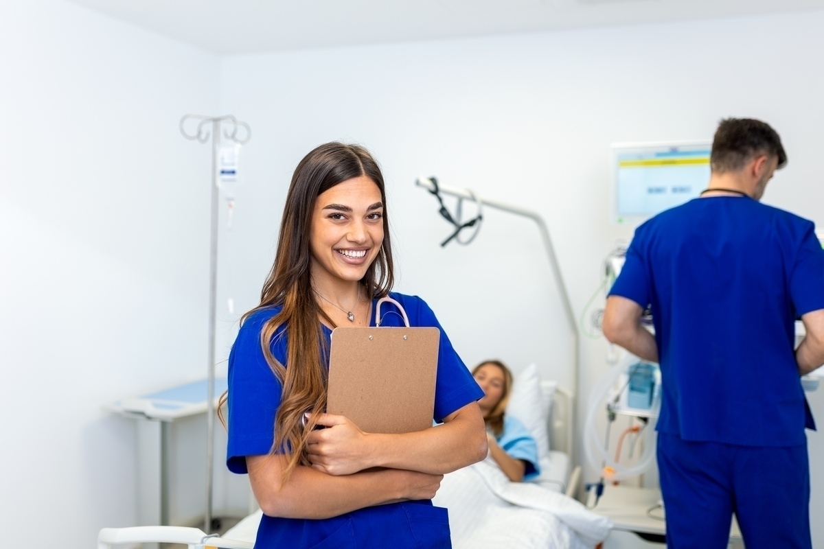 Confident CNA in blue scrubs holding a clipboard while working at a hospital — representing CNA jobs in Brooklyn across clinical healthcare settings