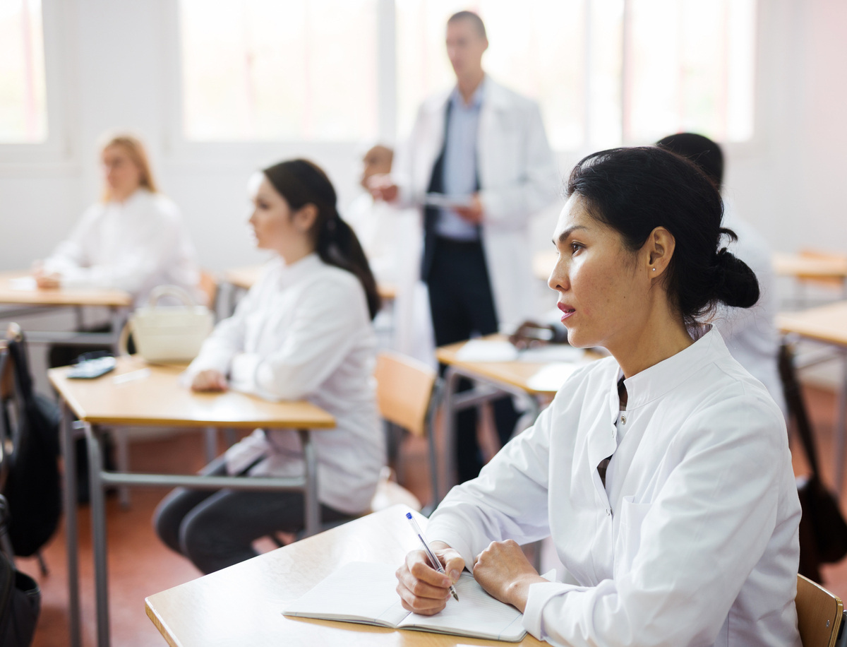 Healthcare students taking notes during medical assistant classes in NYC with an instructor at the front of the classroom