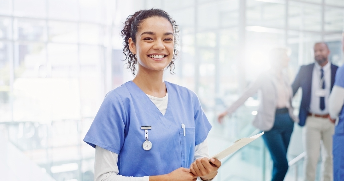 A confident healthcare professional in blue scrubs holding a tablet in a hospital corridor representing a CNA career in Brooklyn