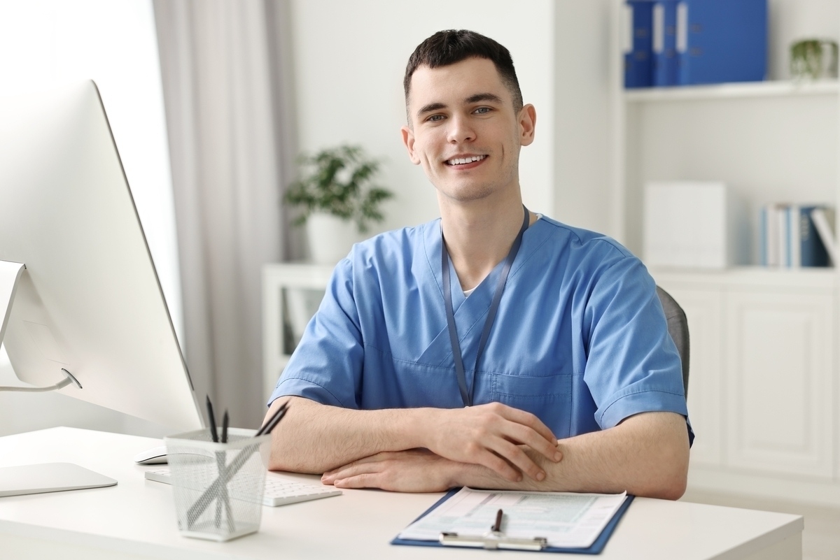 A confident medical assistant in blue scrubs sitting at a desk with a computer representing medical assistant career growth in a professional office setting