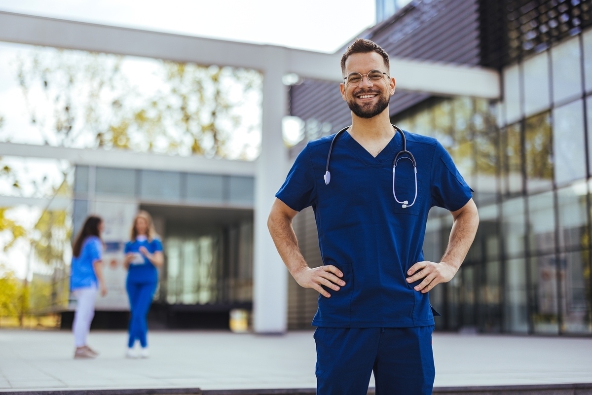 A confident medical assistant in scrubs with a stethoscope standing outside a healthcare facility representing medical assistant hiring in NYC