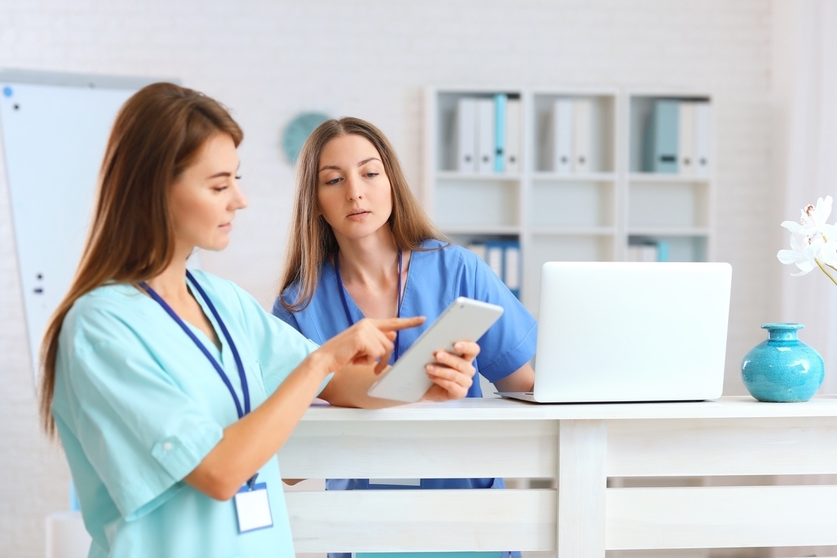 Two healthcare professionals in different colored scrubs collaborating at a desk representing the medical assistant vs nurse distinction in a clinical setting