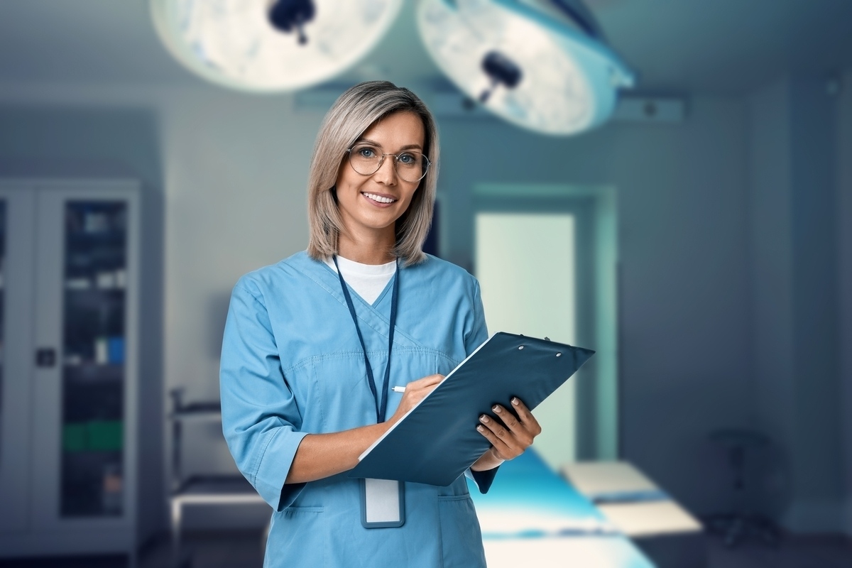 A confident medical assistant in blue scrubs holding a clipboard in a clinical setting representing medical assistant work in NYC across various healthcare environments